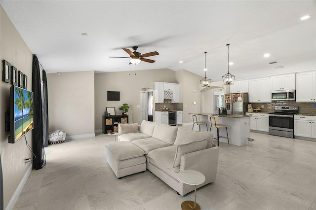 living room featuring arched walkways, marble finish floor, a ceiling fan, vaulted ceiling, and baseboards