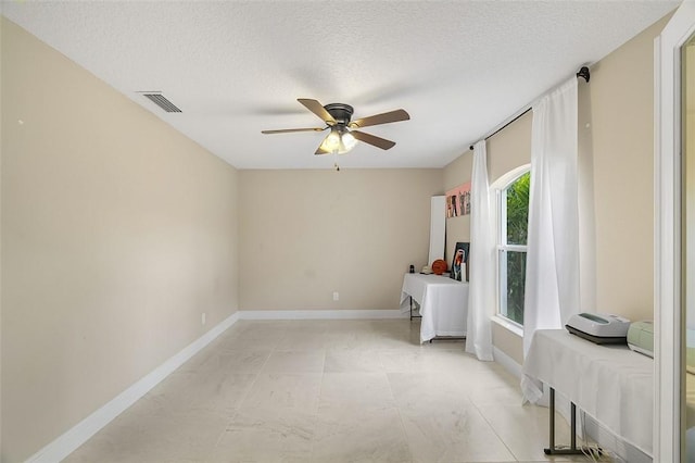 interior space featuring a ceiling fan, baseboards, visible vents, and a textured ceiling