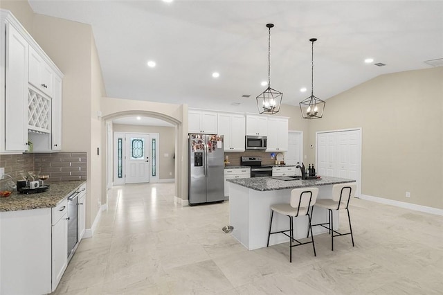 kitchen with arched walkways, lofted ceiling, appliances with stainless steel finishes, a kitchen island with sink, and white cabinetry