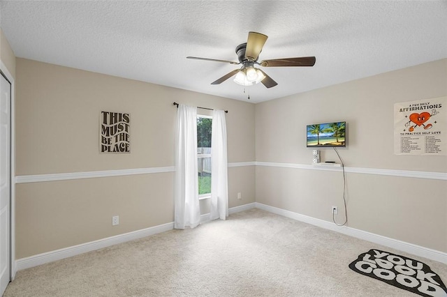 spare room featuring a textured ceiling, carpet floors, a ceiling fan, and baseboards