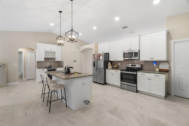 kitchen with arched walkways, appliances with stainless steel finishes, a breakfast bar area, marble finish floor, and vaulted ceiling