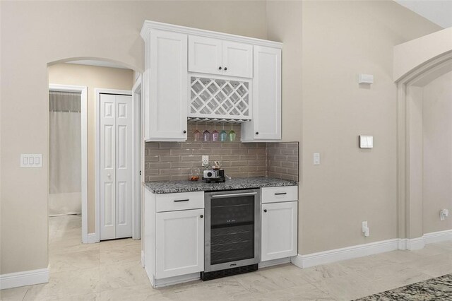 kitchen with arched walkways, beverage cooler, white cabinets, marble finish floor, and dark stone counters