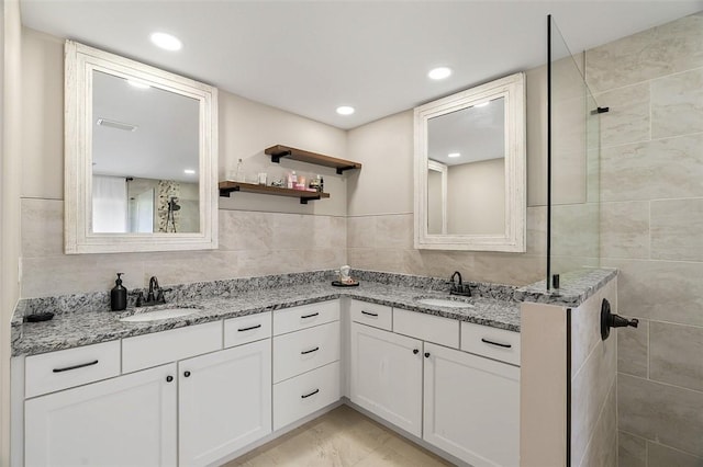 full bathroom featuring tiled shower, a sink, tile walls, and double vanity