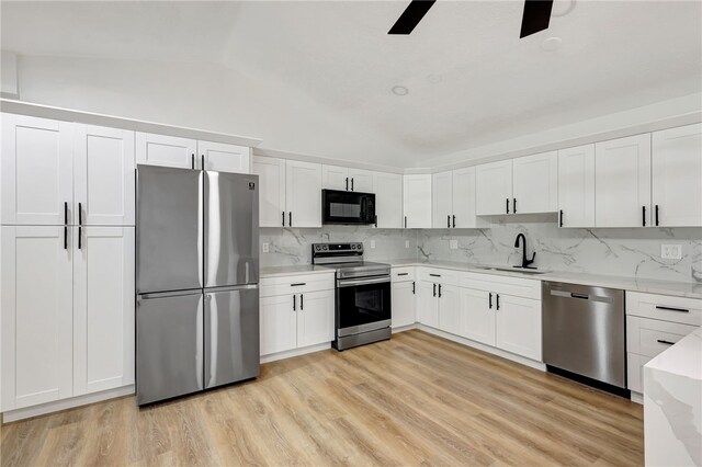 kitchen featuring lofted ceiling, white cabinets, sink, light wood-type flooring, and appliances with stainless steel finishes