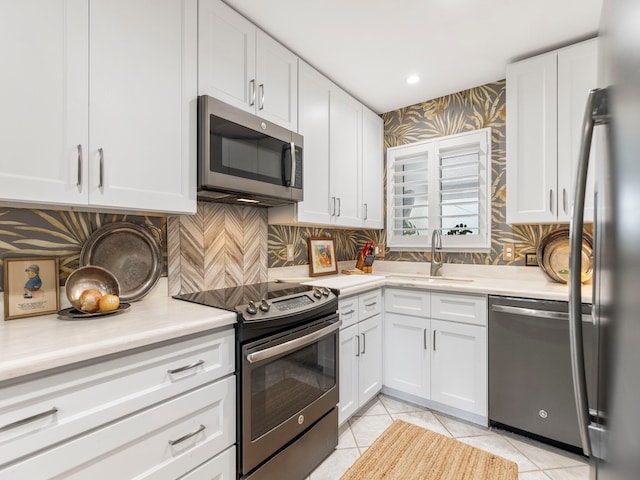 kitchen featuring appliances with stainless steel finishes, sink, light tile patterned floors, and white cabinets