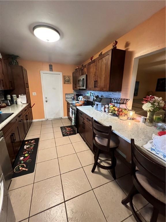 kitchen featuring a kitchen bar, appliances with stainless steel finishes, kitchen peninsula, light stone countertops, and light tile patterned floors