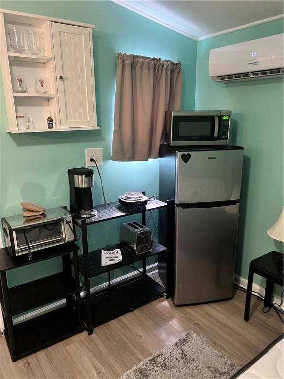 kitchen featuring light hardwood / wood-style floors, an AC wall unit, ornamental molding, and appliances with stainless steel finishes