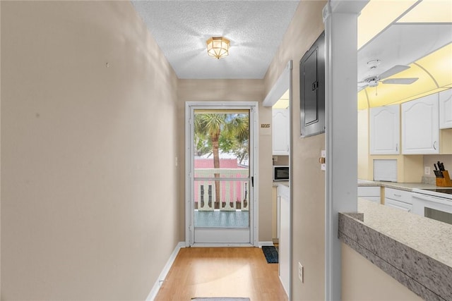 entryway featuring light wood finished floors, baseboards, a ceiling fan, and a textured ceiling