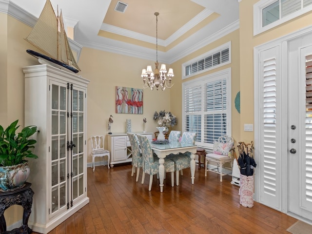 dining space with dark wood-type flooring, a tray ceiling, an inviting chandelier, and ornamental molding