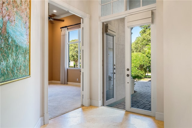 doorway featuring light carpet, ceiling fan, and crown molding