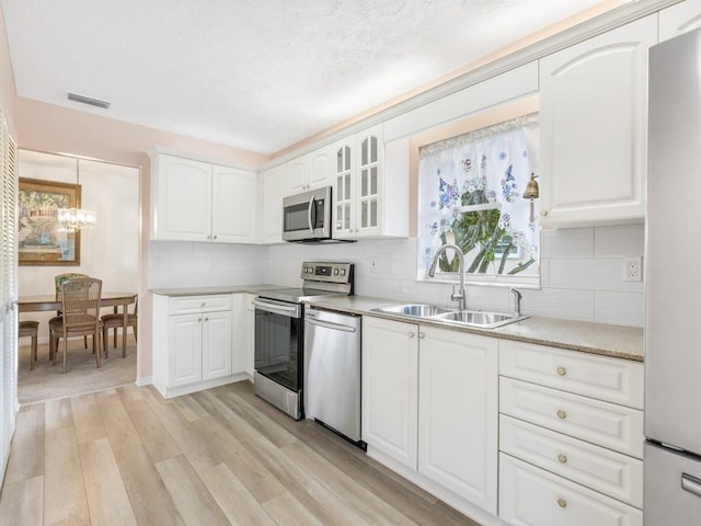 kitchen featuring sink, hanging light fixtures, appliances with stainless steel finishes, light hardwood / wood-style floors, and white cabinets