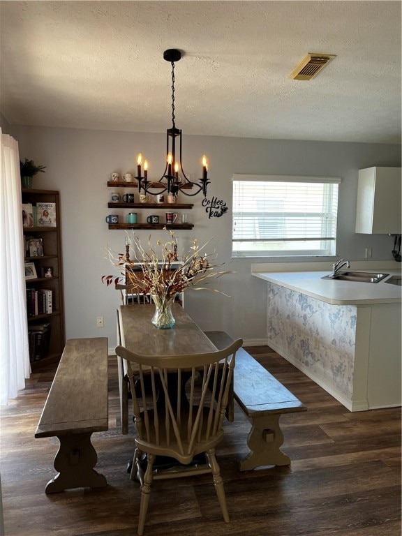 dining area featuring dark wood-type flooring, an inviting chandelier, sink, and a textured ceiling