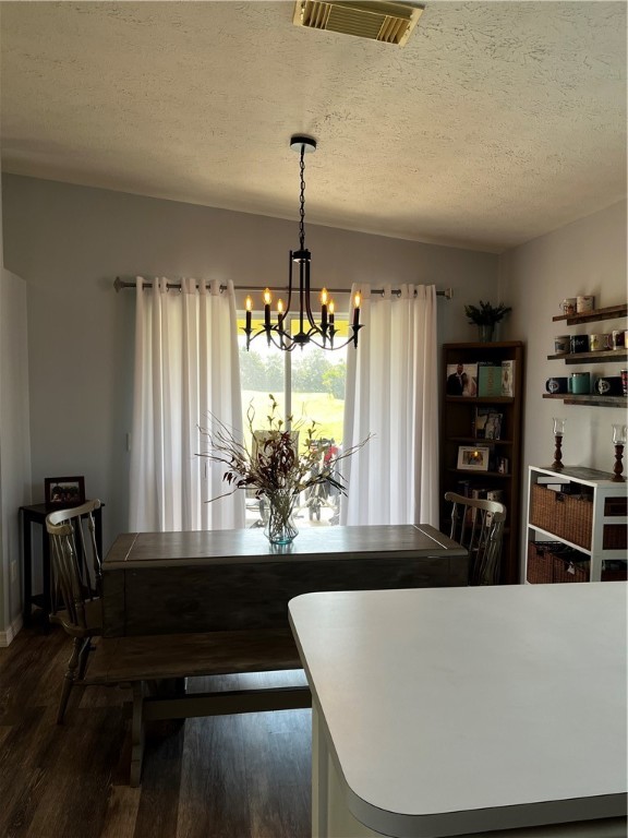 dining room featuring dark wood-type flooring, a textured ceiling, and a notable chandelier