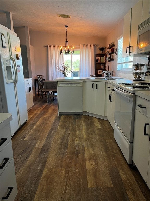 kitchen featuring kitchen peninsula, dark hardwood / wood-style floors, white appliances, a notable chandelier, and pendant lighting