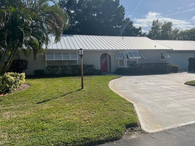 ranch-style house with stucco siding, concrete driveway, a front yard, a standing seam roof, and metal roof