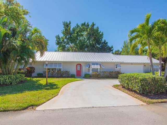 ranch-style home with a front yard, driveway, stucco siding, a garage, and metal roof