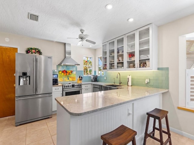 kitchen featuring visible vents, a sink, premium appliances, light stone counters, and wall chimney exhaust hood