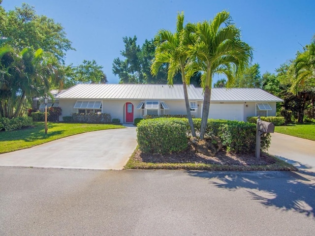 ranch-style house featuring stucco siding, a front yard, metal roof, and driveway