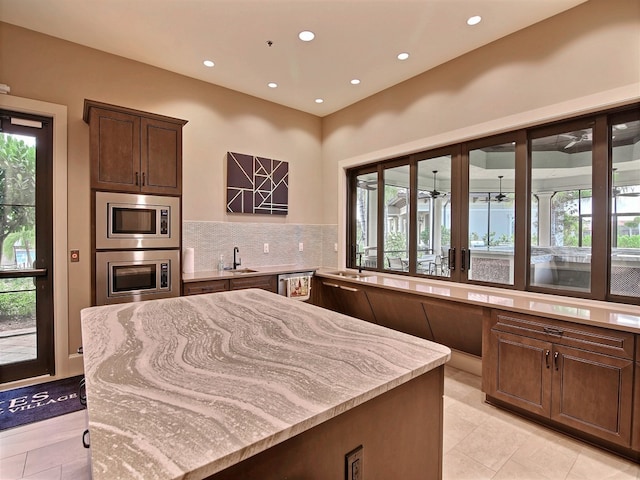 kitchen with stainless steel appliances, dark brown cabinetry, sink, light stone counters, and decorative backsplash