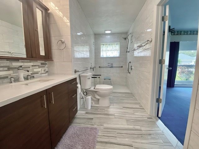 bathroom featuring a shower, tile walls, toilet, and vanity