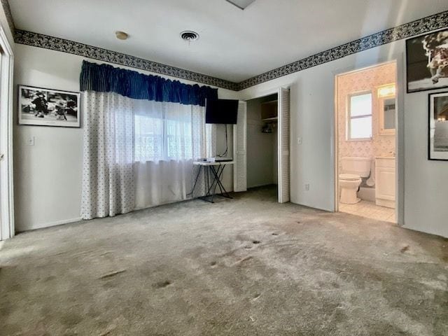 unfurnished bedroom with ensuite bathroom, carpet flooring, and multiple windows