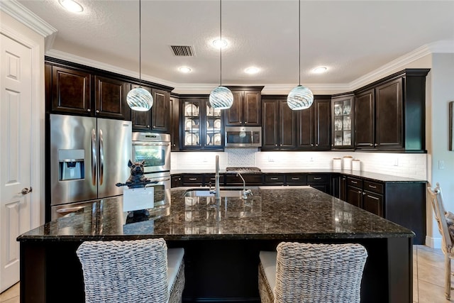 kitchen featuring decorative light fixtures, dark brown cabinetry, stainless steel appliances, and an island with sink