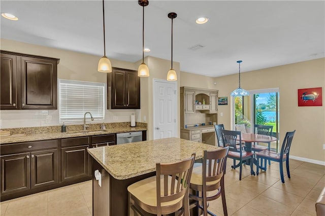 kitchen featuring a center island, sink, stainless steel dishwasher, decorative light fixtures, and a kitchen bar