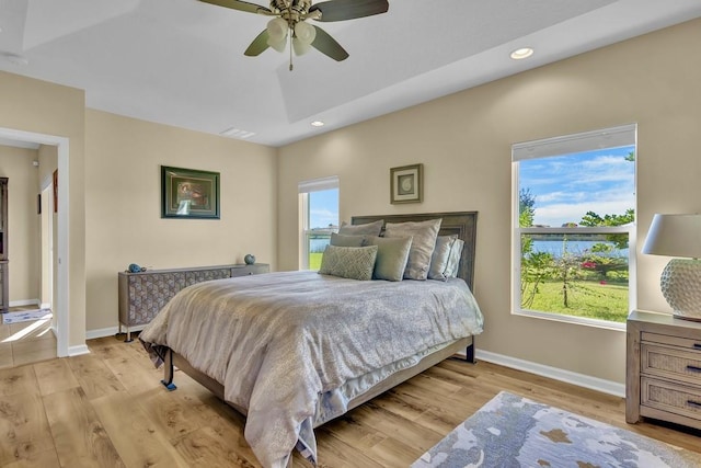 bedroom with ceiling fan, a raised ceiling, and light hardwood / wood-style flooring