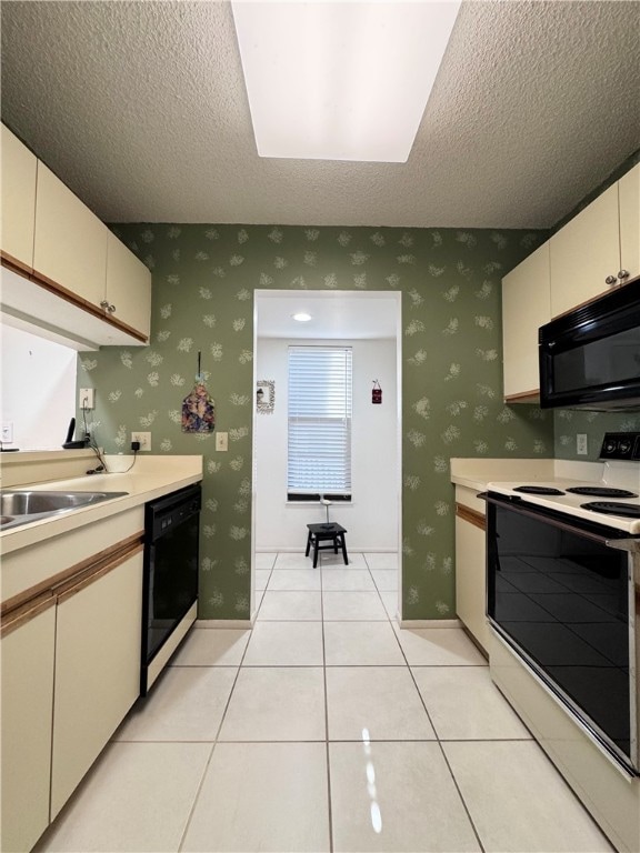 kitchen with cream cabinets, light tile patterned floors, black appliances, and a textured ceiling