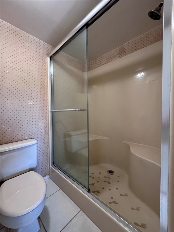 bathroom featuring tile patterned floors, toilet, and a shower with door