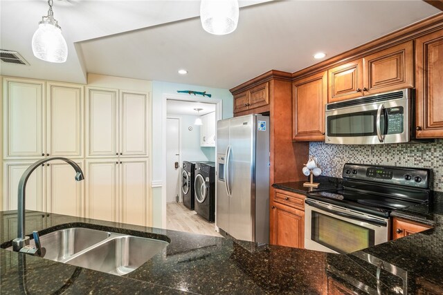 kitchen with light hardwood / wood-style floors, sink, appliances with stainless steel finishes, decorative light fixtures, and washer and clothes dryer