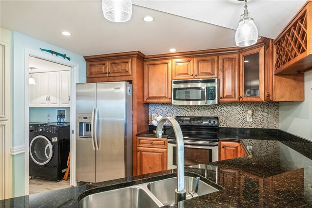 kitchen featuring stainless steel appliances, dark stone counters, washer / clothes dryer, pendant lighting, and light hardwood / wood-style flooring