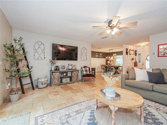 living room featuring ceiling fan with notable chandelier and a textured ceiling