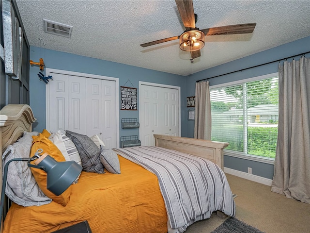 bedroom featuring a textured ceiling, carpet floors, ceiling fan, and multiple closets