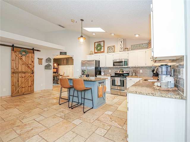 kitchen with a center island, decorative backsplash, a barn door, appliances with stainless steel finishes, and decorative light fixtures