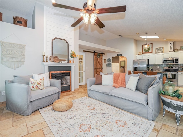 living room featuring a textured ceiling, a barn door, ceiling fan, and lofted ceiling