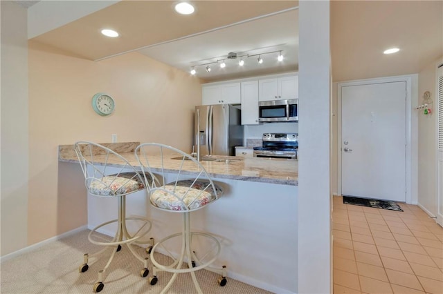 kitchen featuring light stone countertops, recessed lighting, a peninsula, white cabinets, and stainless steel appliances