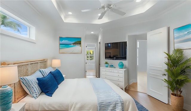 bedroom featuring a tray ceiling, light hardwood / wood-style flooring, and multiple windows