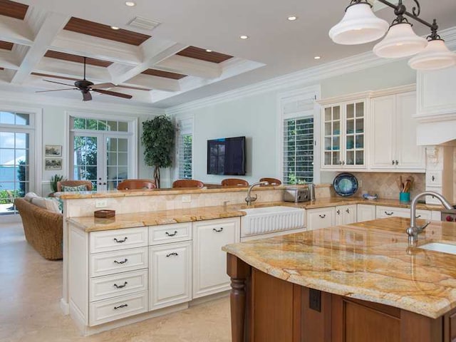 kitchen featuring sink, a kitchen island with sink, hanging light fixtures, light stone counters, and french doors