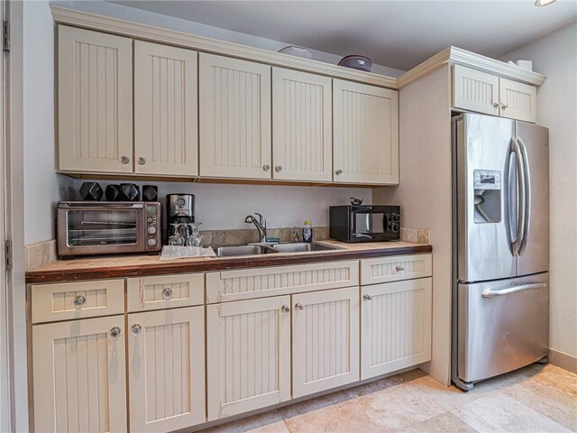 kitchen with butcher block countertops, stainless steel refrigerator with ice dispenser, sink, and cream cabinetry