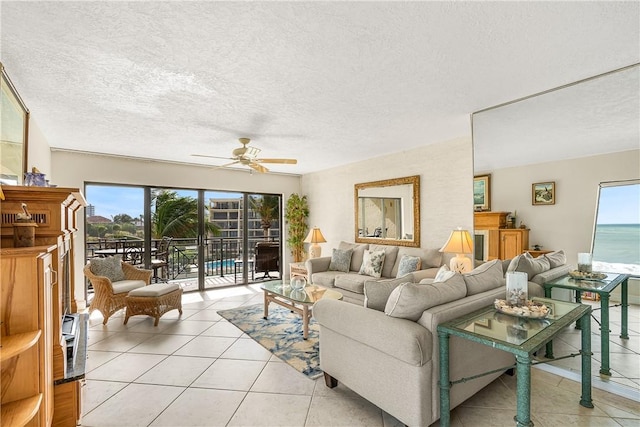 living room with ceiling fan, a water view, light tile patterned floors, and a textured ceiling