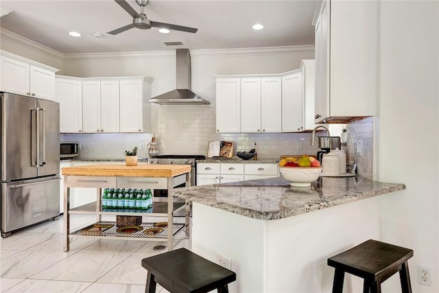 kitchen with wall chimney exhaust hood, stainless steel appliances, light stone counters, decorative backsplash, and white cabinets