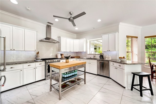 kitchen with white cabinetry, sink, stainless steel appliances, wall chimney range hood, and dark stone counters