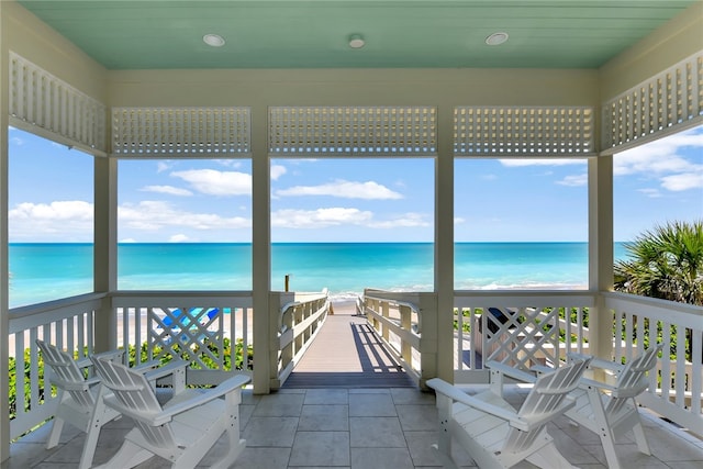 unfurnished sunroom featuring a water view and a view of the beach