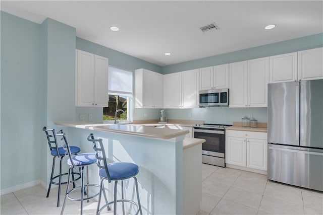 kitchen featuring light tile patterned floors, a breakfast bar, appliances with stainless steel finishes, white cabinets, and kitchen peninsula