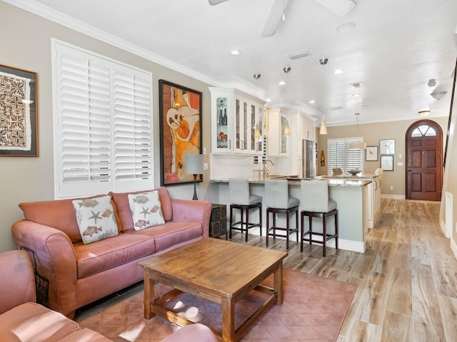 living room featuring ceiling fan, sink, light hardwood / wood-style floors, and ornamental molding