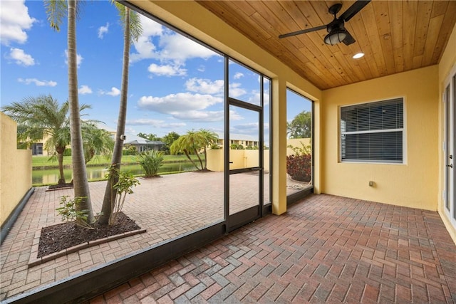 unfurnished sunroom with ceiling fan, a water view, and wooden ceiling