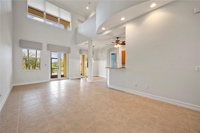 unfurnished living room featuring ceiling fan, light tile patterned flooring, a towering ceiling, and sink