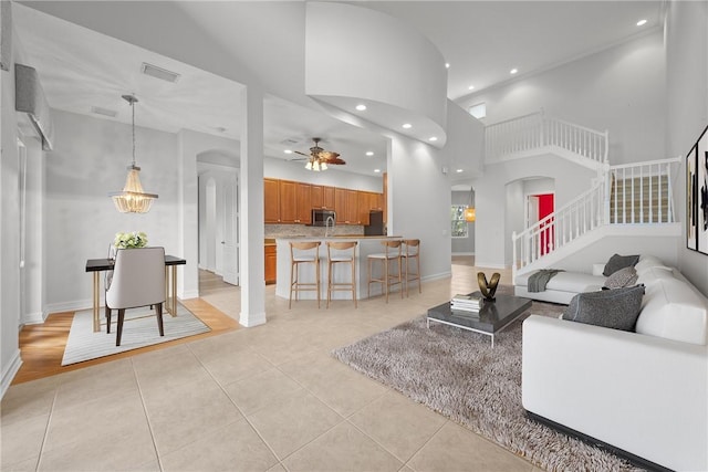 living room with ceiling fan with notable chandelier, light tile patterned flooring, and a high ceiling