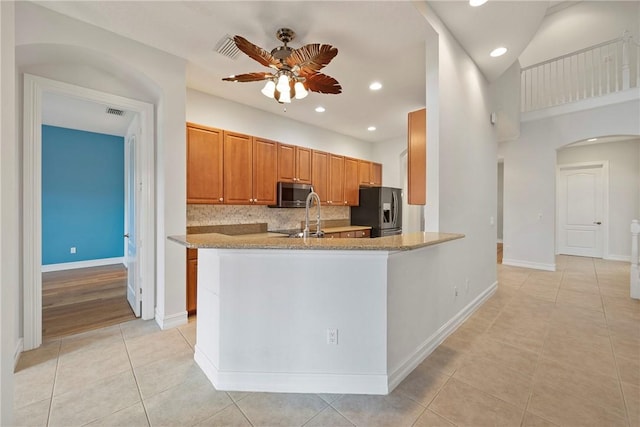 kitchen with kitchen peninsula, light stone counters, stainless steel appliances, ceiling fan, and light tile patterned floors